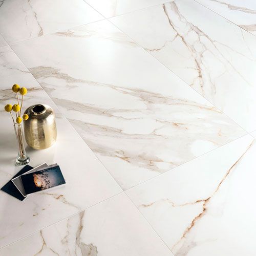 Immagine ravvicinata del pavimento serie Charme colore Gold, con oggetti e fotografie posati su un pavimento in gres con effetto marmo bianco e venature dorate