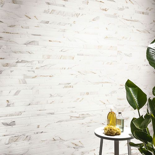 Particolare ravvicinato del rivestimento di un bagno, serie Charme colore Gold, con una pianta e uno sgabello con portasapone