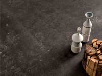 Copertina serie Belgica. Still life del pagimento nero con alcuni oggetti in ceramica e legna da ardere appoggiati sul pavimento.