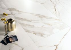 Immagine ravvicinata di un pavimento della collezione "Charme", effetto marmo Gold con alcuni oggetti posati su di esso e un riflesso di luce