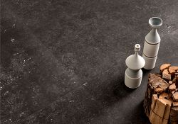 Copertina serie Belgica. Still life del pagimento nero con alcuni oggetti in ceramica e legna da ardere appoggiati sul pavimento.